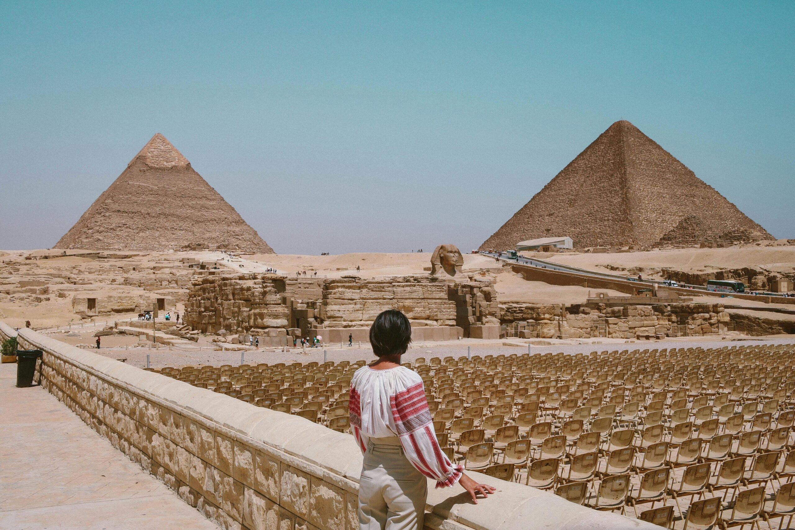 A tourist admires the Great Pyramids and Sphinx in Giza, Egypt under the clear daytime sky.