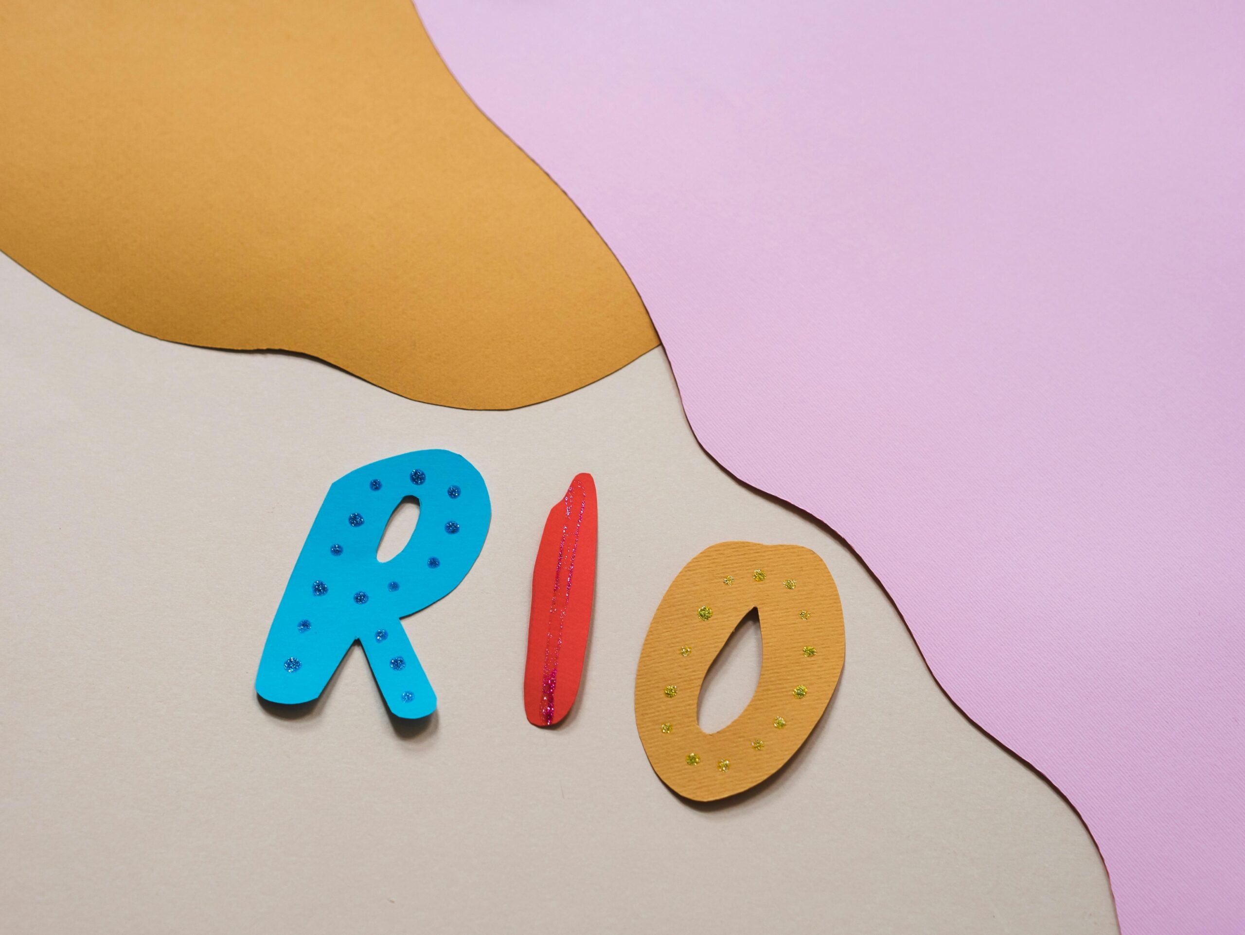 Colorful paper cutout design featuring the word 'Rio' in vibrant letters against a pastel background.